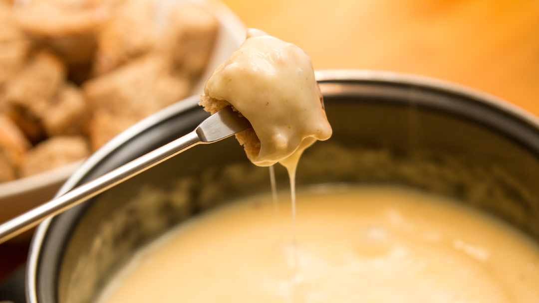 Frisch eingetauchtes Brotwürfel auf Fonduegabel mit geschmolzenem Käse, Kunst des Fonduetauchens